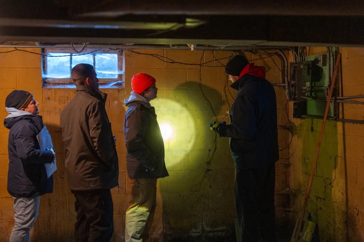 Students inspecting a basement wall with a flashlight on an on-site inspection